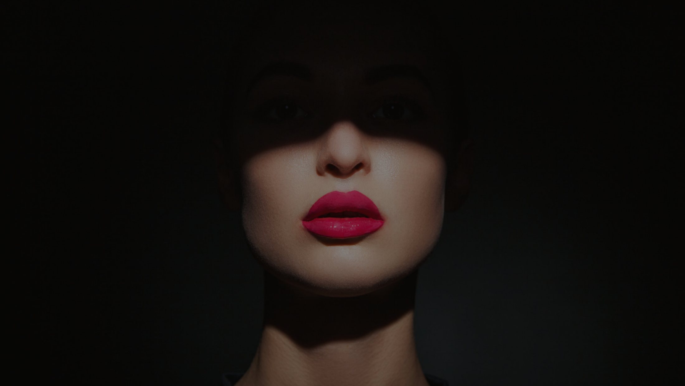 A face half in shadow, lips in pink, seen through the slot of a door