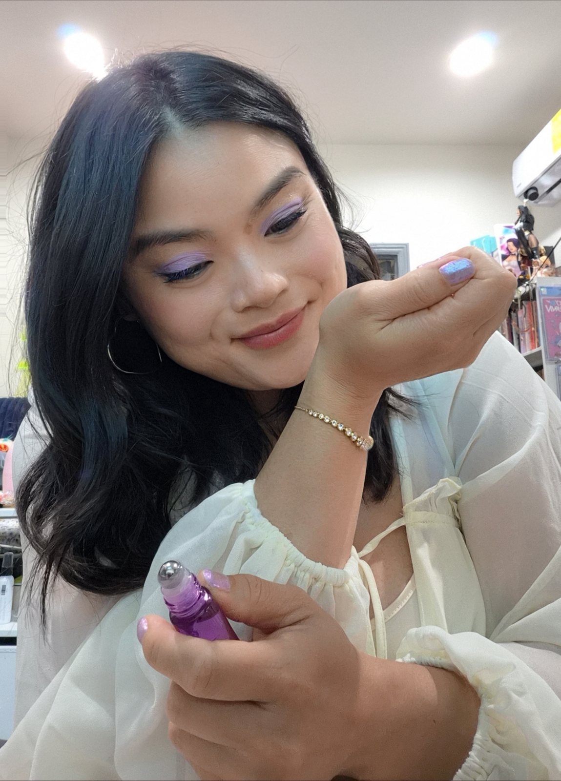 A woman smiling as she smells a perfume roller on her wrist